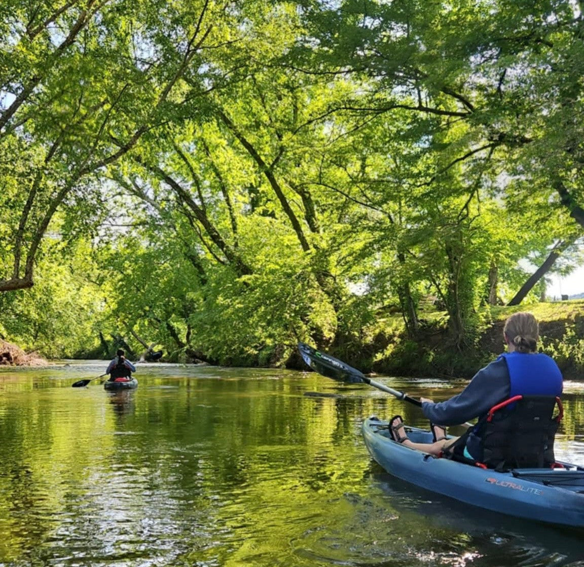 Two people kayaking on a calm Yadkin Rver with green trees lining the banks